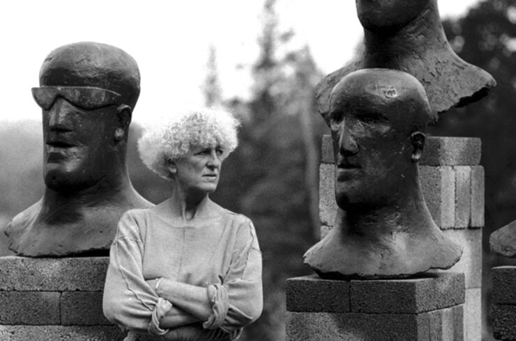 Elisabeth Frink standing with Goggle and Tribute heads, Woolland House grounds, 1984. Image © Christine Fauto/ Artist © in Elisabeth Frink images courtesy of Bree and Tully Jammet/ Courtesy of Dorset History Centre.